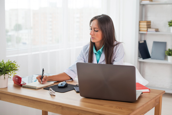 Portrait of physician doctor working in medical office workplace writing prescription sitting at desk.